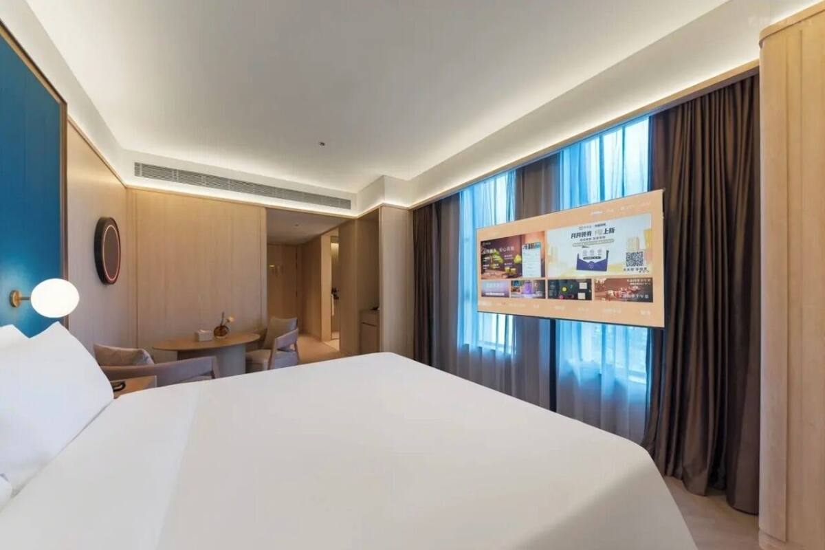 Une chambre d’hôtel avec un grand lit, un bureau, une chaise, un écran de télévision et une fenêtre avec des rideaux.