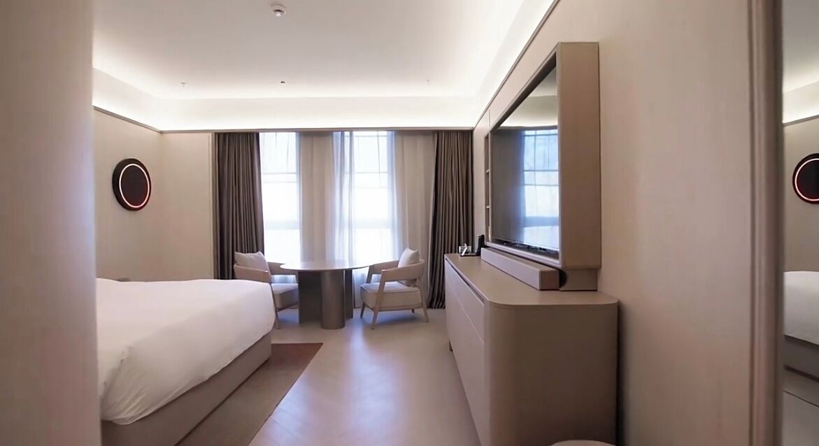 Ein Hotelzimmer mit einem Bett, einem Schreibtisch, einem Sessel, einem Fernseher und einem großen Fenster.