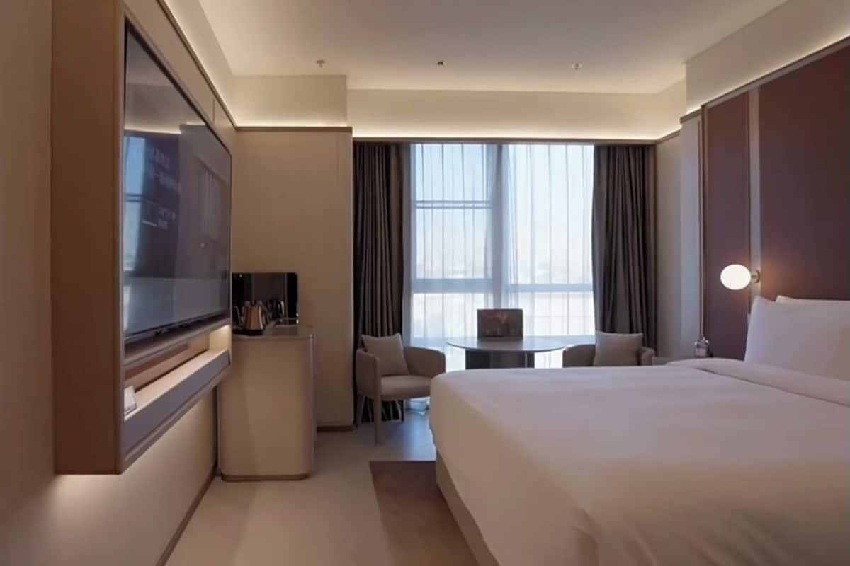 Une chambre d’hôtel avec un lit, un bureau, une chaise, une télévision et une grande fenêtre.