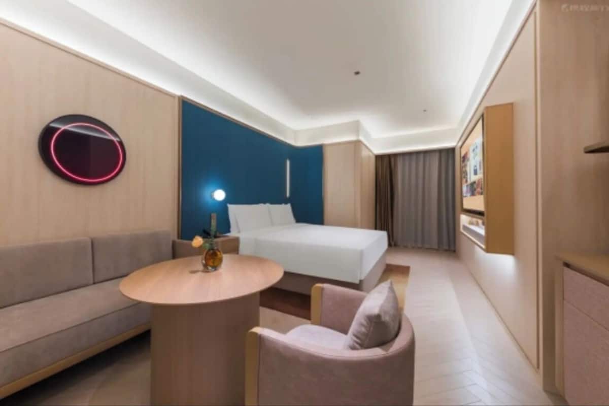 Une chambre d’hôtel moderne, équipée d’un lit, d’un canapé, d’une table ronde et d’un luminaire circulaire fixé au mur.