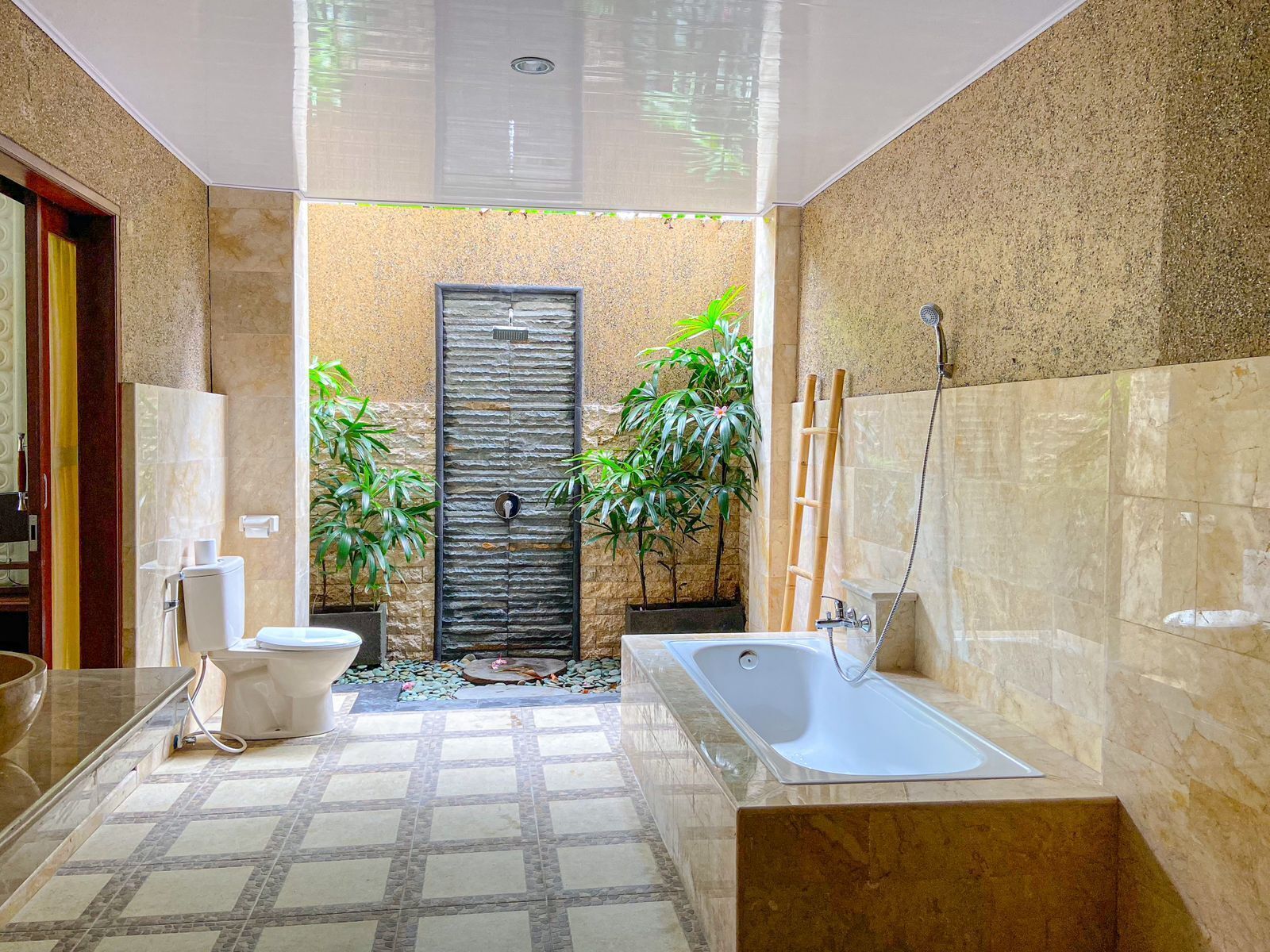 A modern bathroom with a bathtub, toilet, and sink. There are plants and a shower area.