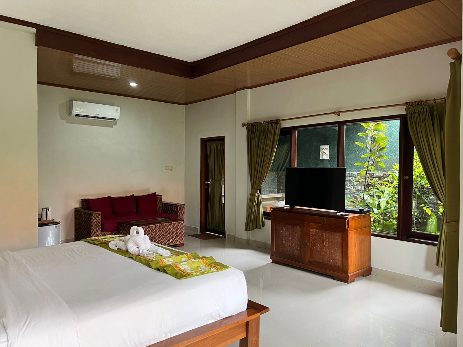 A hotel room with a bed, a television, a wooden desk, a wicker sofa, and a window with curtains.