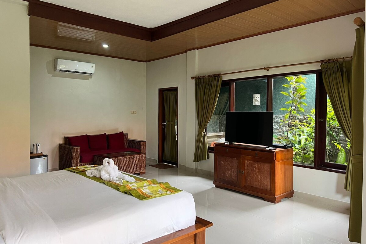 A hotel room with a bed, a television, a wooden desk, a wicker sofa, and a window with curtains.