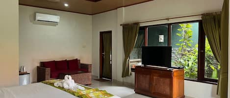 A hotel room with a bed, a television, a wooden desk, a wicker sofa, and a window with curtains.