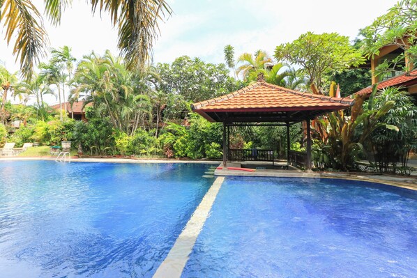 A swimming pool with a tiled roof structure, surrounded by lush greenery and palm trees.