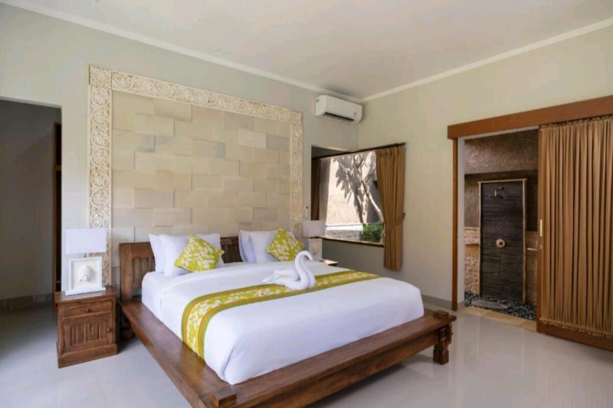 A hotel room with a large bed, a nightstand, a wardrobe, and a window with a view of palm trees.