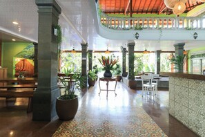 A spacious lobby with a high ceiling, a balcony with a railing, and potted plants.
