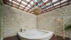 A stone-walled room with a wooden deck, a hot tub, and a bamboo ladder. - Three Brothers Bungalows and Villas (Legian)
