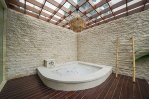 A stone-walled room with a wooden deck, a hot tub, and a bamboo ladder. - Three Brothers Bungalows and Villas (Legian)