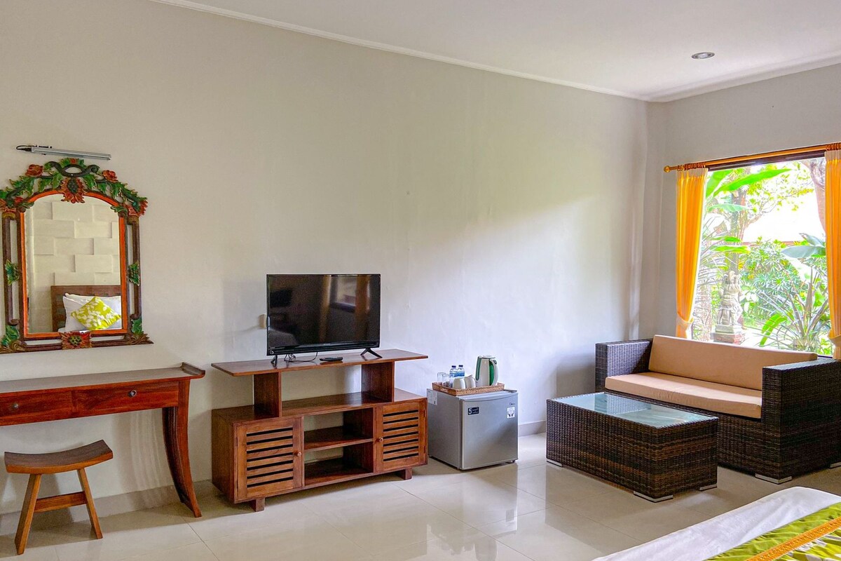 A room with a TV on a wooden stand, a small fridge, a sofa, a dining table, and a chair.