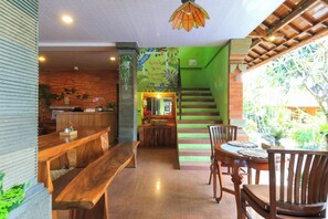 A restaurant with a wooden bench seating area, a counter, and a staircase leading to a green area with plants. - Three Brothers Bungalows and Villas (Legian)
