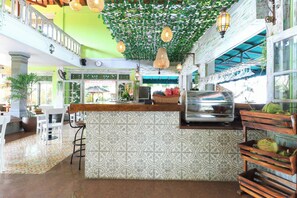 A restaurant with a patterned wall, a wooden counter, hanging lights, and a view of the street. - Three Brothers Bungalows and Villas (Legian)