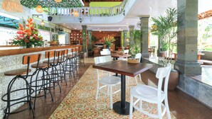 A spacious indoor area with a bar, multiple seating arrangements, and a balcony with greenery.