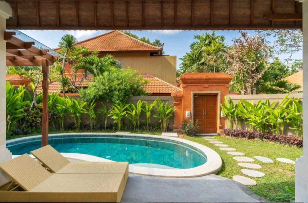 A pool area with lounge chairs, a stone pathway, and tropical vegetation.