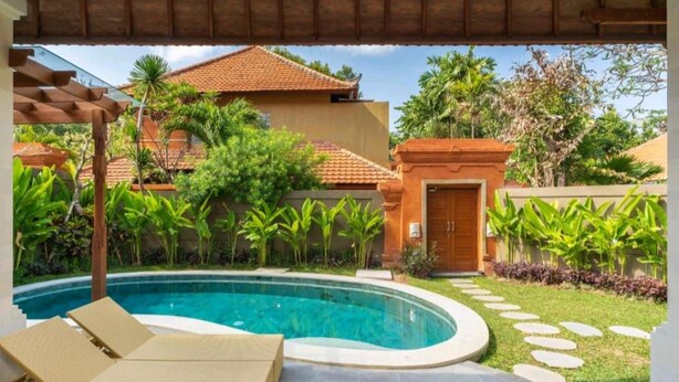 A pool area with lounge chairs, a stone pathway, and tropical vegetation.