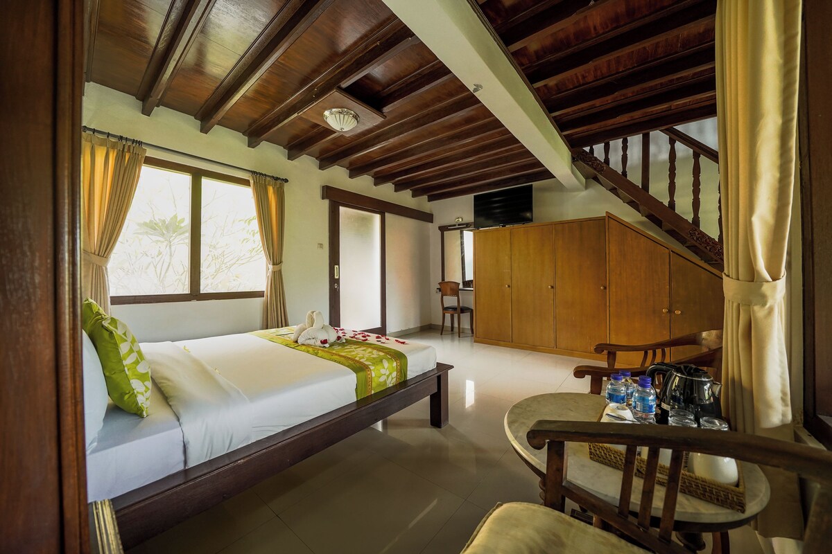 A hotel room with a bed, a dining table with chairs, a wardrobe, and a staircase.