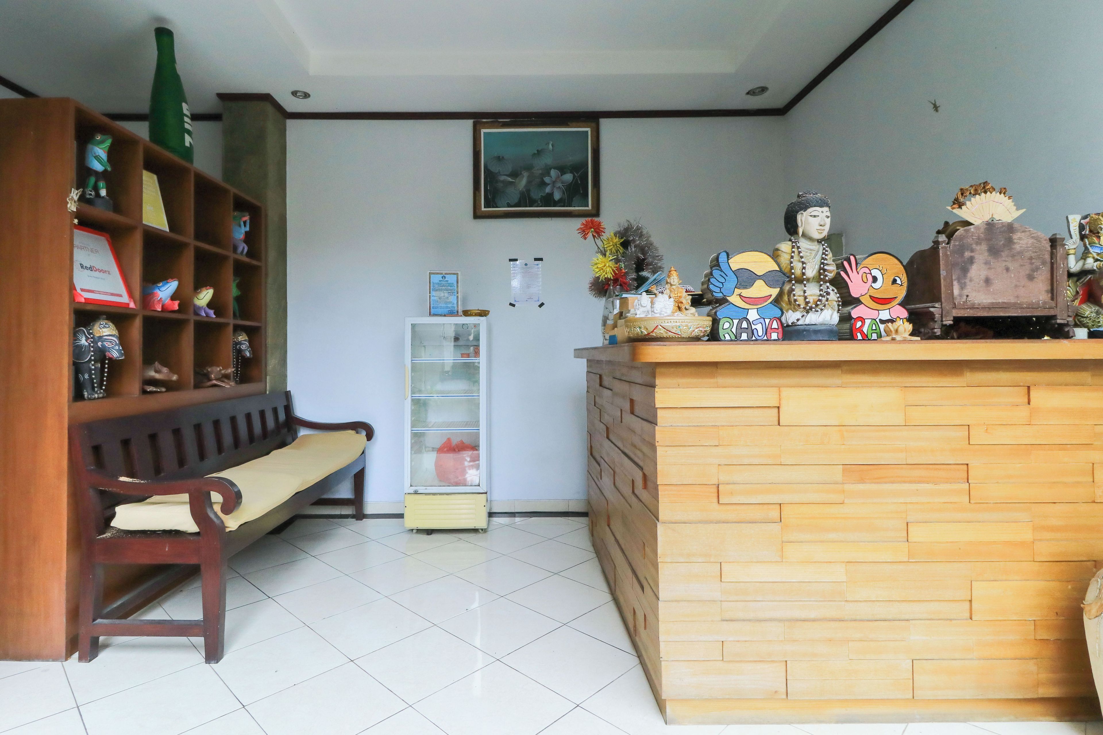 A reception desk with a wooden finish, a bench, a shelf with various items, and a framed picture on the wall.