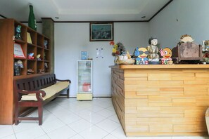A reception desk with a wooden finish, a bench, a shelf with various items, and a framed picture on the wall. - Three Brothers Bungalows and Villas (Legian)