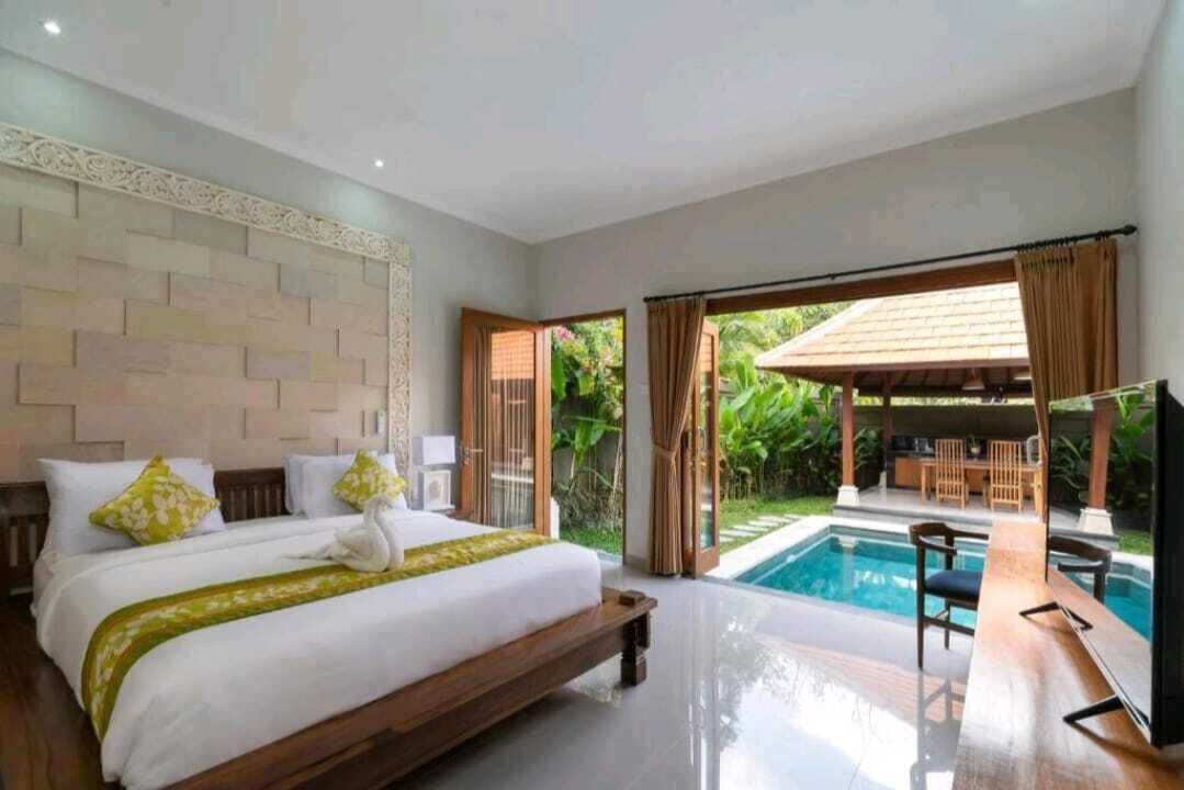 A bedroom with a large bed, a TV, and a view of an outdoor pool area.