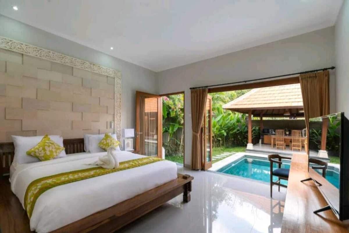 A bedroom with a large bed, a TV, and a view of an outdoor pool area.