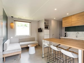 Eine moderne Küche mit Holztischplatte, weißen Barhocker, integriertem Mikrowellenherd und einer Sitzecke mit Sofa und kleinem runden Tisch.