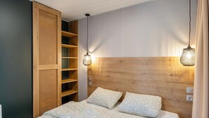 Ein Schlafzimmer mit Holz-Kopfteil, einem Bett mit gemusterten Betttextilien, einer eingebauten Regallösung und Pendelleuchten.
