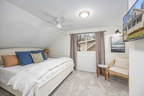 A bedroom with a bed, a ceiling fan, a window with curtains, a small table, and a sofa.