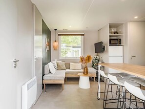 Ein gemütlicher, kompakter Wohnbereich mit Küchenzeile, einer Couch, einem Esstisch mit Stühlen und einem Fernseher.