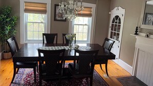 Une salle à manger avec un lustre, une table en bois, des chaises et un tapis à motifs.