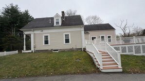 Une maison à deux étages avec un porche à l’avant, un escalier et une clôture blanche en bois.