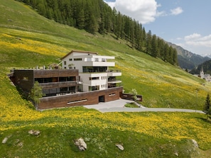 Ein modernes mehrgeschossiges Gebäude mit Balkonen, gelegen an einem Hang mit einer Wiese voller gelber Blumen.