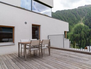 Eine moderne Terrasse im Freien mit einem Holztisch und -stühlen, mit Blick auf ein bewaldetes Tal.