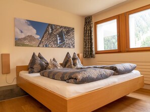 Ein Schlafzimmer mit einem hölzernen Bett, gemusterten Kissen, einem Wandbild und einem Fenster mit Vorhängen.