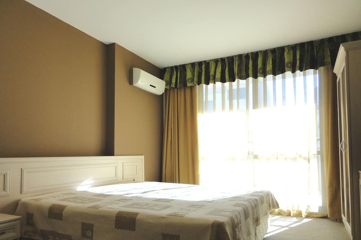 Ein Hotelzimmer mit Bett, Nachttisch, Wand-Klimaanlage und einem Vorhangfenster.