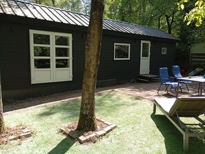 Une petite cabane avec une véranda, deux chaises, une table et un arbre dans la cour.