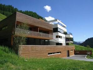 Un immeuble moderne à plusieurs étages, doté de lambris en bois horizontaux, de balcons et offrant une vue dégagée sur le paysage verdoyant environnant.