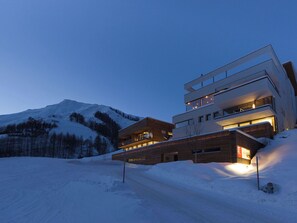 Un bâtiment moderne à plusieurs étages, doté d’une façade en bois et de balcons, situé dans une région montagneuse enneigée.