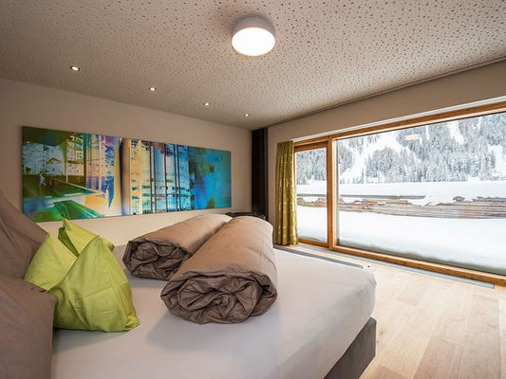 Un dormitorio moderno con un ventanal grande, una cama con almohadas y un cuadro en la pared.