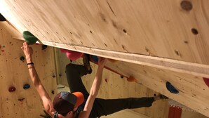 Una persona arrampica su un muro di legno con appigli di diversi colori.