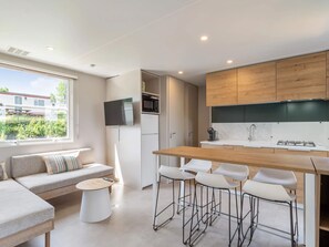 Eine moderne Küche mit Holzarbeitsplatte, weißen Barhocker, Backofen und an der Wand montiertem Fernseher.