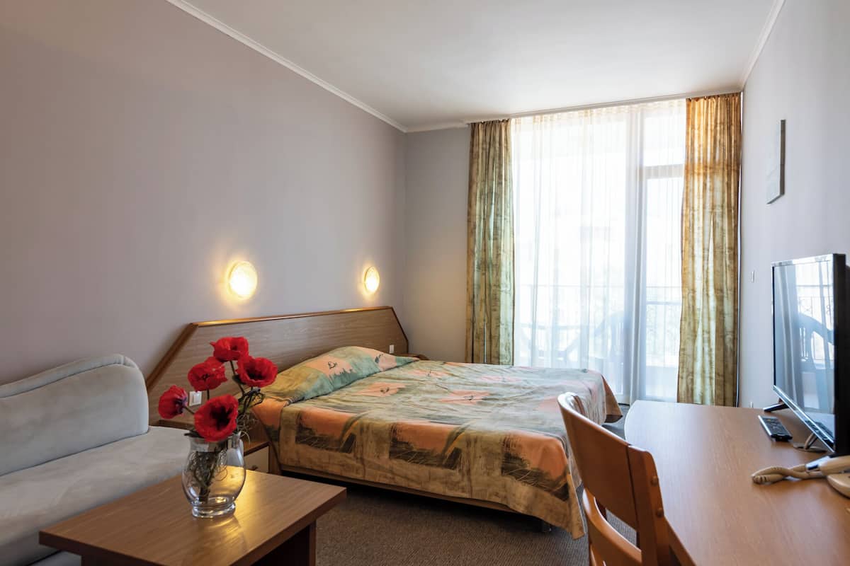 Ein Hotelzimmer mit Bett, Sofa, Tisch, Fernseher und einem Fenster mit Vorhängen.