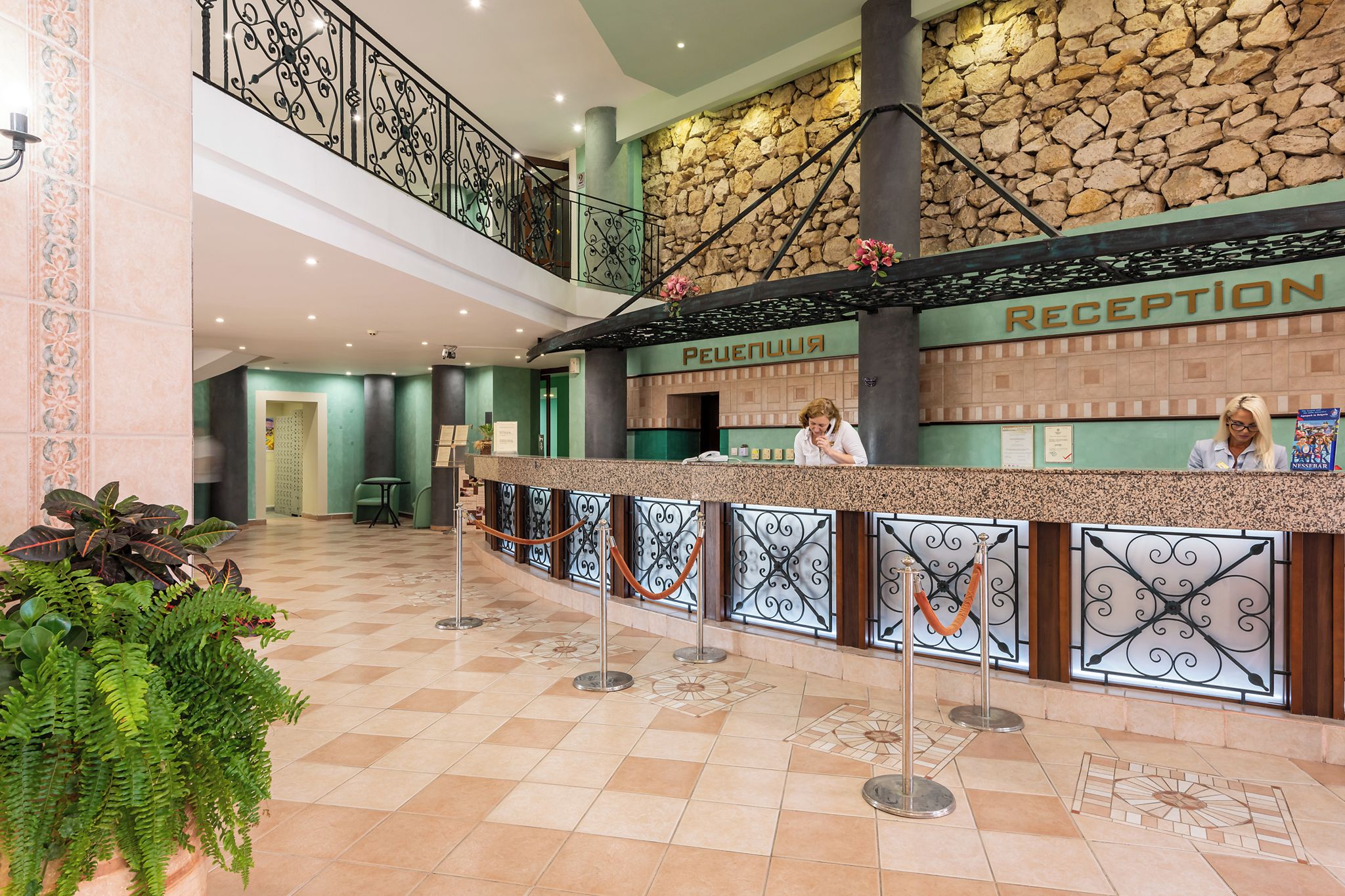 Una recepción con pared de piedra, mostrador de registro y una escalera que sube a un nivel superior.