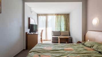 Habitación de hotel con cama, escritorio con computadora, televisor, sofá y ventana con cortinas.