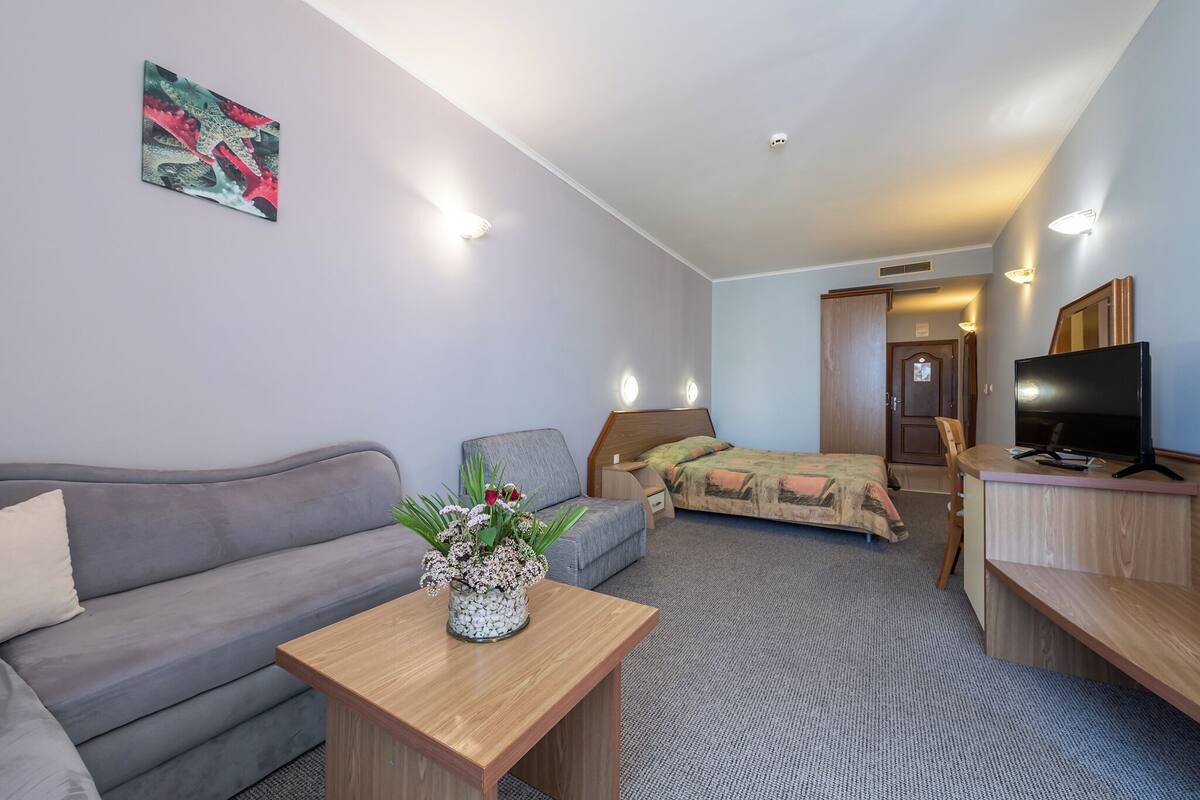 A hotel room with a sofa, a bed, a desk, a TV, and a painting on the wall.