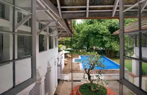 A covered outdoor area with a pool, a small tree, and a view of a garden. - Neemrana's- Tower House (Kochi)