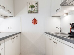A modern kitchen with white cabinetry, a stainless steel sink, and a red hanging pot rack. - Atlantis Apartments by MEIN SAMNAUN – MOUNTAIN HOMES, (Samnaun-Ravaisch) by Interhome (Samnaun-Ravaisch)