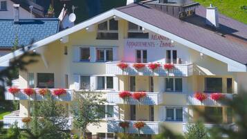 Un immeuble à plusieurs étages doté de balcons ornés de fleurs, portant l’inscription « Atlantis Apartments - Zimmer ».