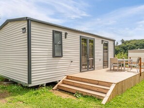 Ein Wohnmobil mit einer Terrasse, Schiebetüren und einem kleinen Tisch mit Stühlen im Freien.