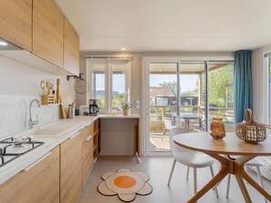 Une cuisine moderne dotée d’une cuisinière à gaz, de meubles blancs et donnant sur une terrasse extérieure.
