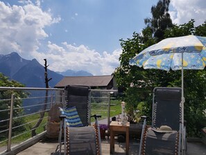 Een terras met uitzicht op bergen, een tafel met een stoel en een patroonrijke parasol.